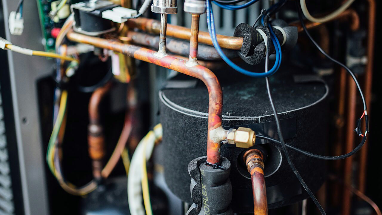 Geöffnetes Innenleben einer Wärmepumpe mit Kupferleitungen und elektrischen Komponenten.